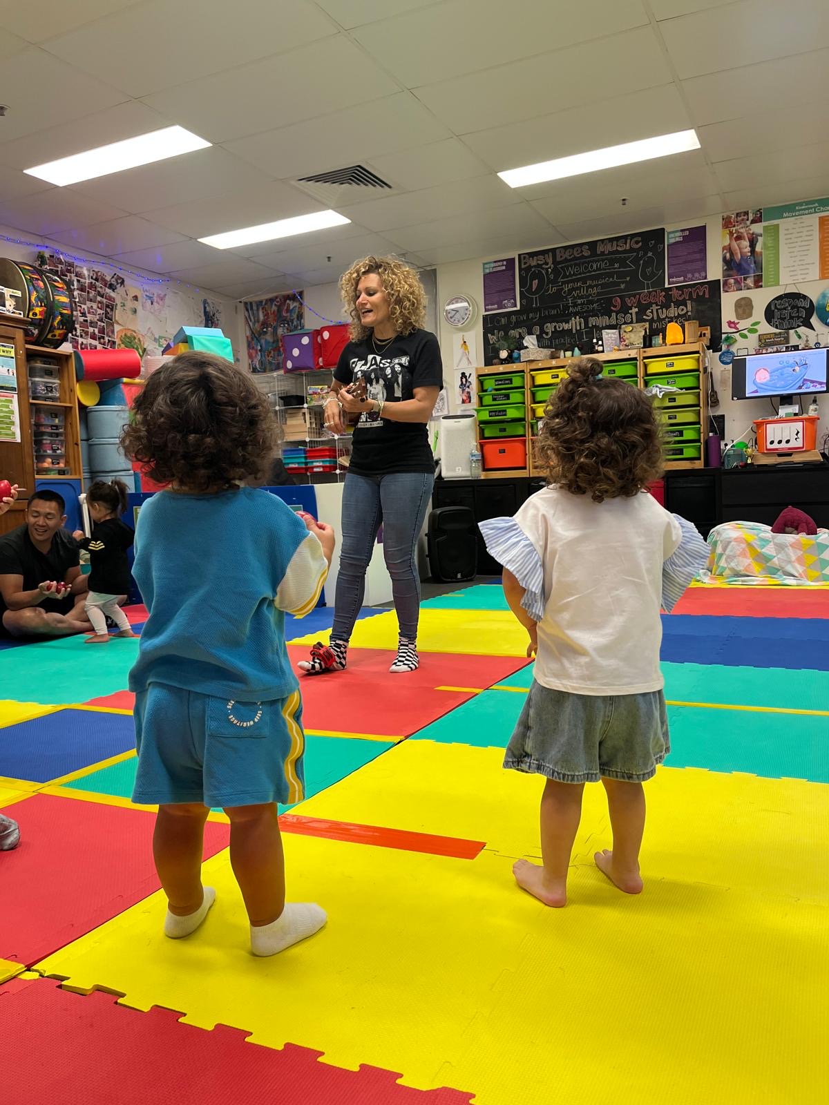 Two children watching miss tania play the ukelele
