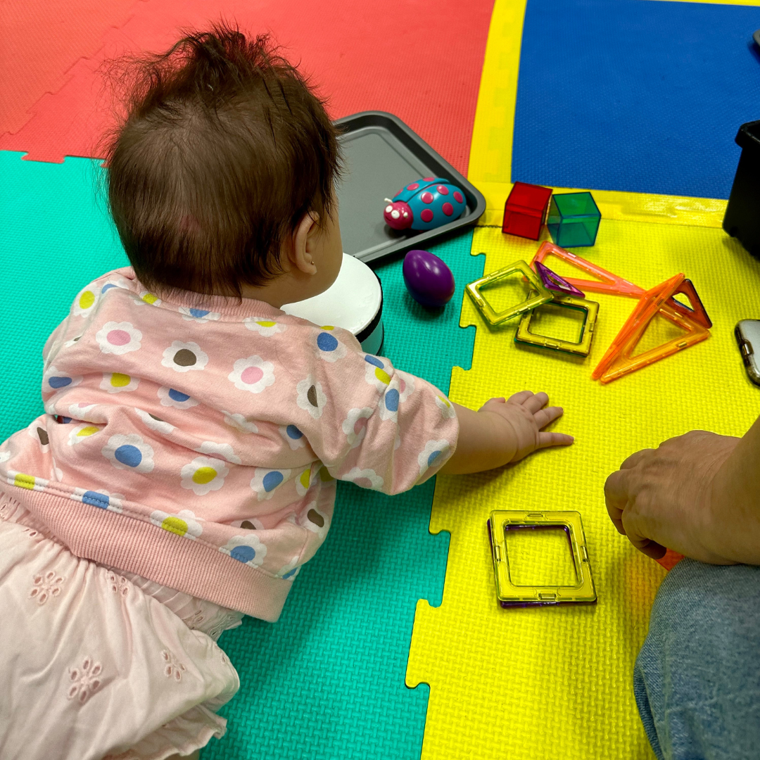 a baby playing with toys in a music class, with a parent close by