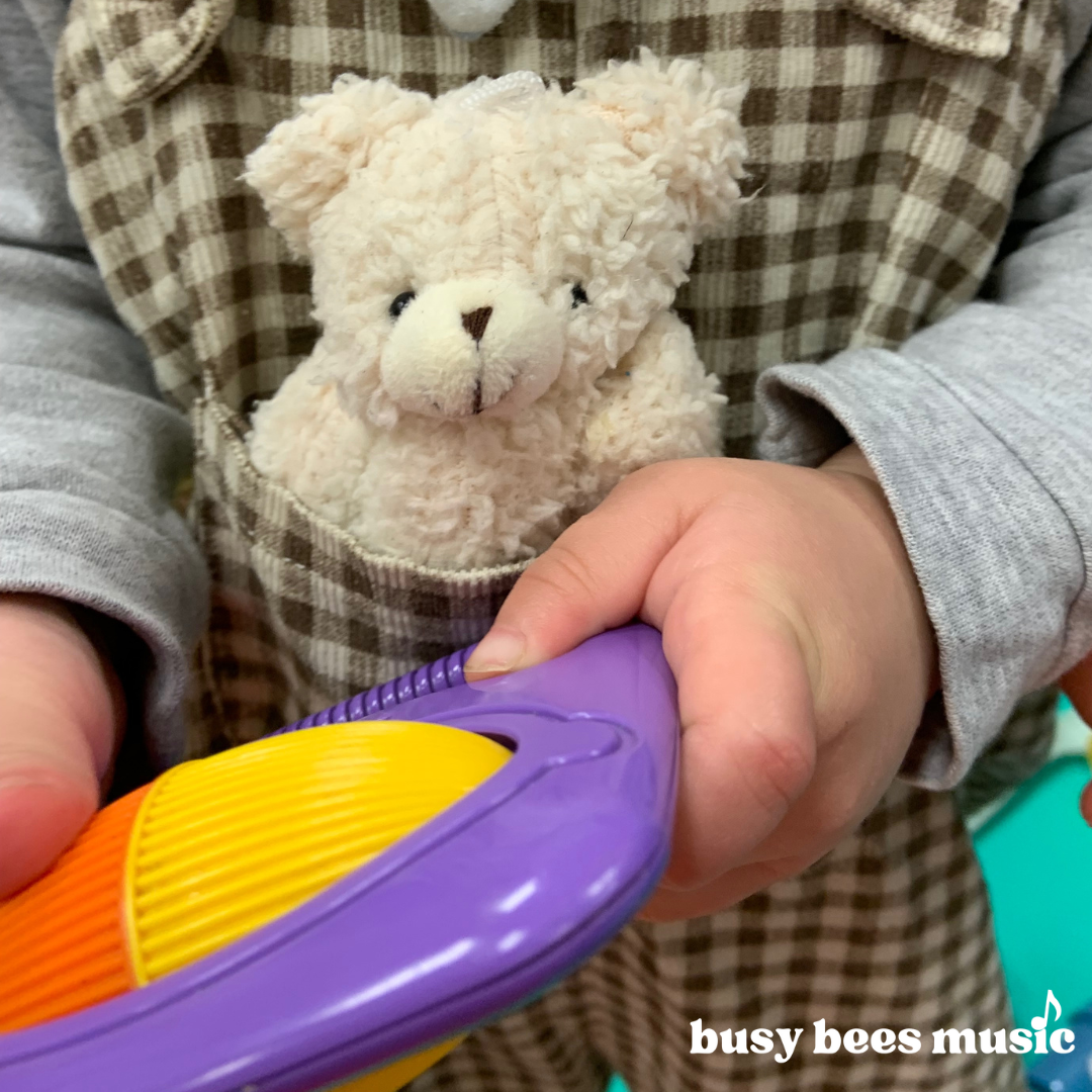 cute picture of a id with a teddy in his pocket, holding an instrument